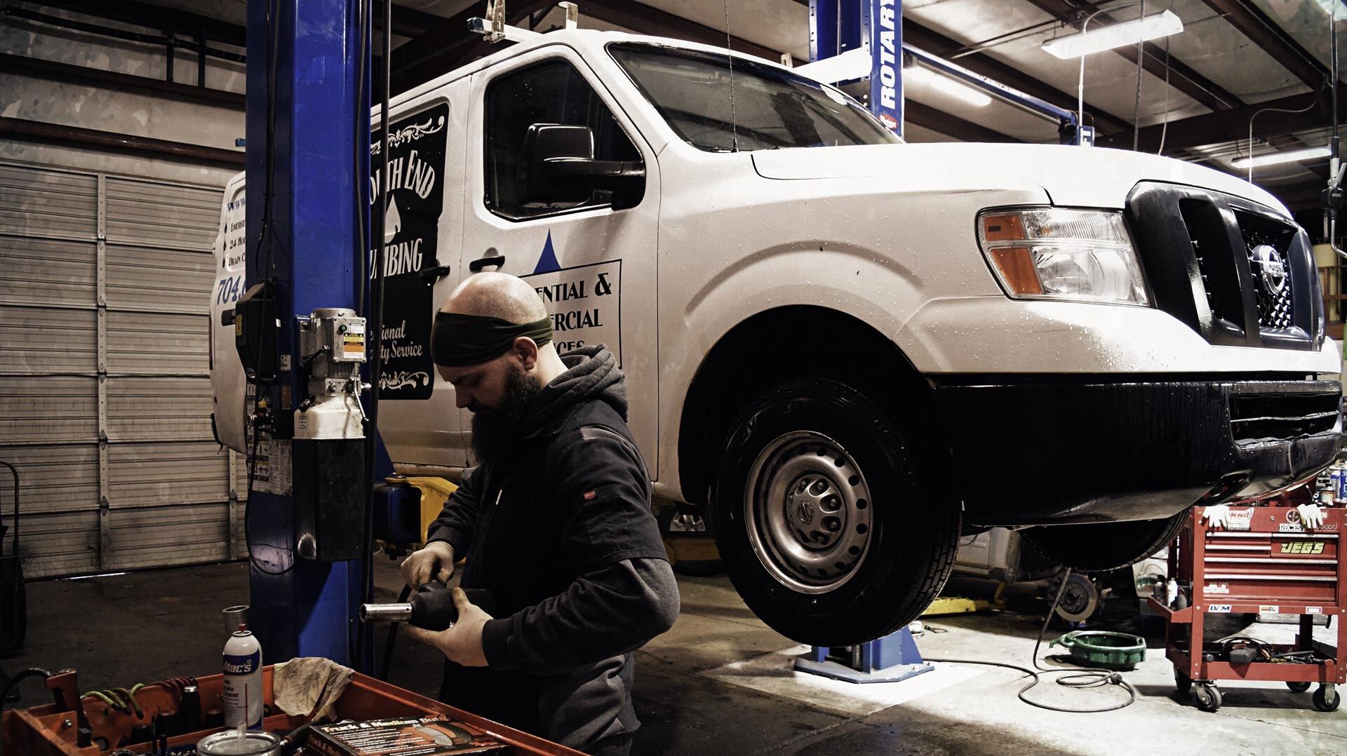 A white work van up on a lift being serviced at Hughes Automotive