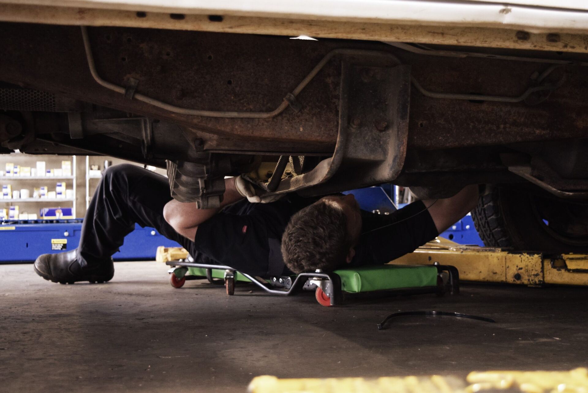 A Hughes technician working underneath a vehicle on a creeper